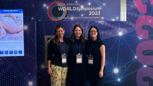 Three recipients of the ThinkGenetic Foundation Pro-GC program standing together in front of a banner for the 2023 WORLD Symposium