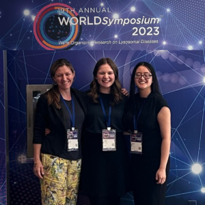 Three recipients of the ThinkGenetic Foundation Pro-GC program standing together in front of a banner for the 2023 WORLD Symposium